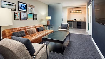 A modern living room with a leather sofa, a glass coffee table, and a kitchen area in the background.