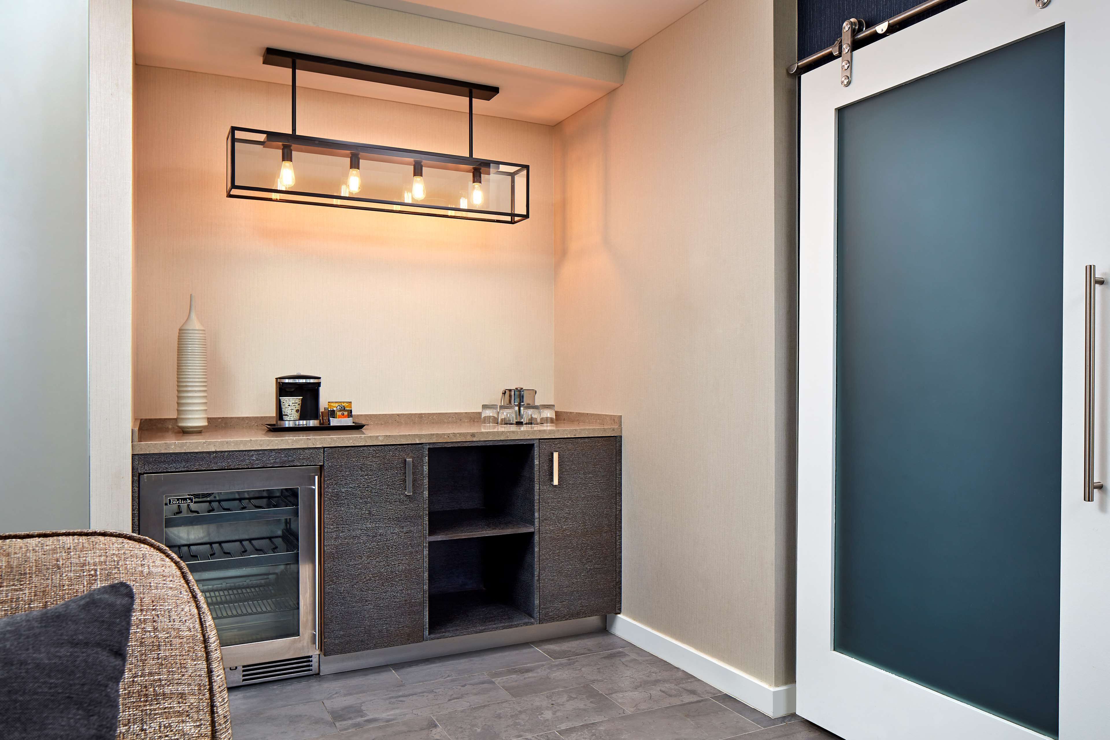 A modern kitchen with a built-in oven, a coffee maker, and a hanging light fixture.
