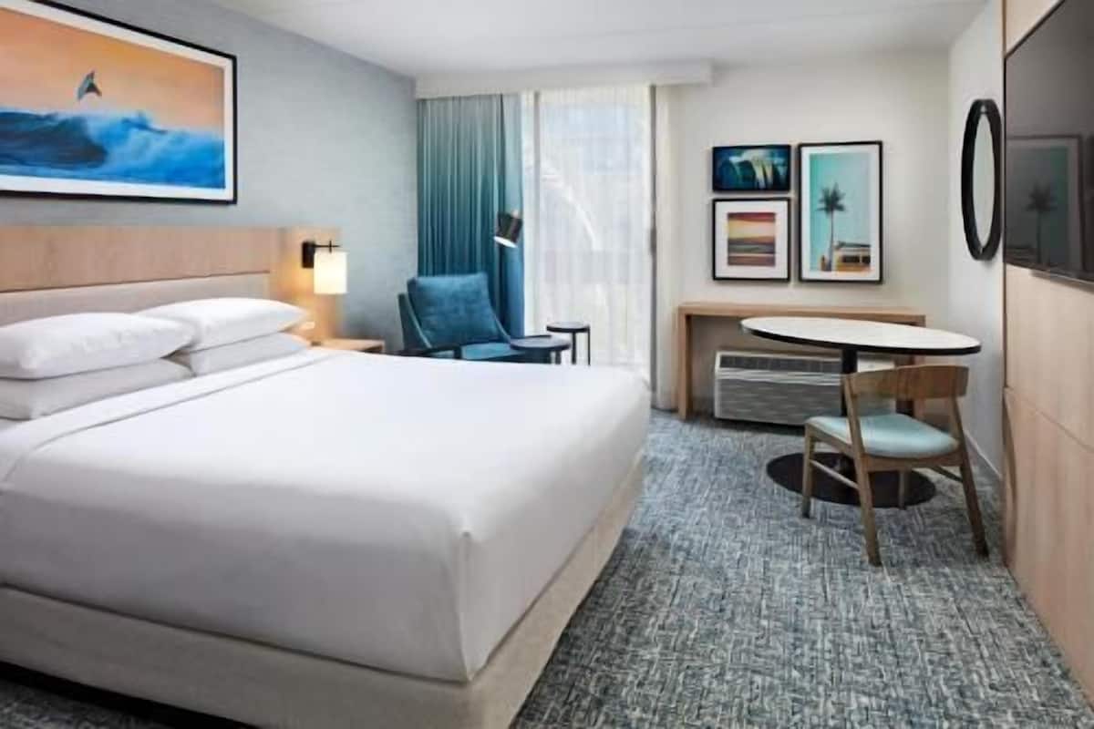 Una habitación de hotel con cama, escritorio, silla, mesita y televisor.