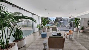 A spacious indoor area with a modern design, featuring a large seating area with a wooden chair, a round table, and potted plants. - Hotel MDR Marina del Rey - a DoubleTree by Hilton (Marina del Rey)
