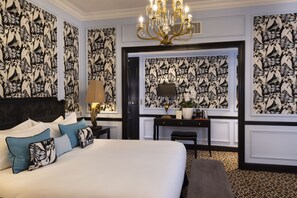 A hotel room with a large bed, a desk, a chair, a TV, and a chandelier. - West End Hotel (Paris)