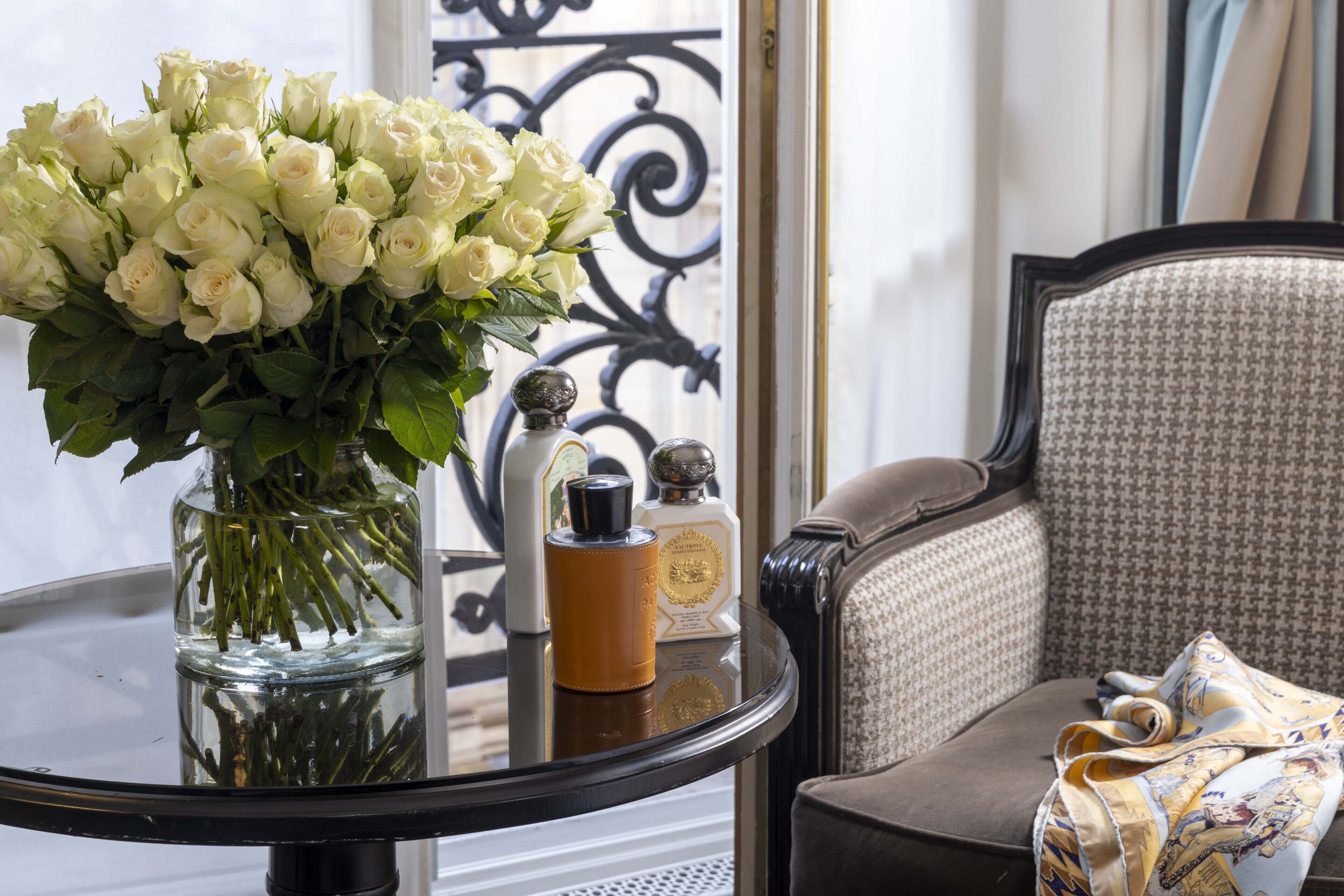 Une table ronde ornée d’un vase de roses blanches, d’un flacon de parfum et d’un objet décoratif.