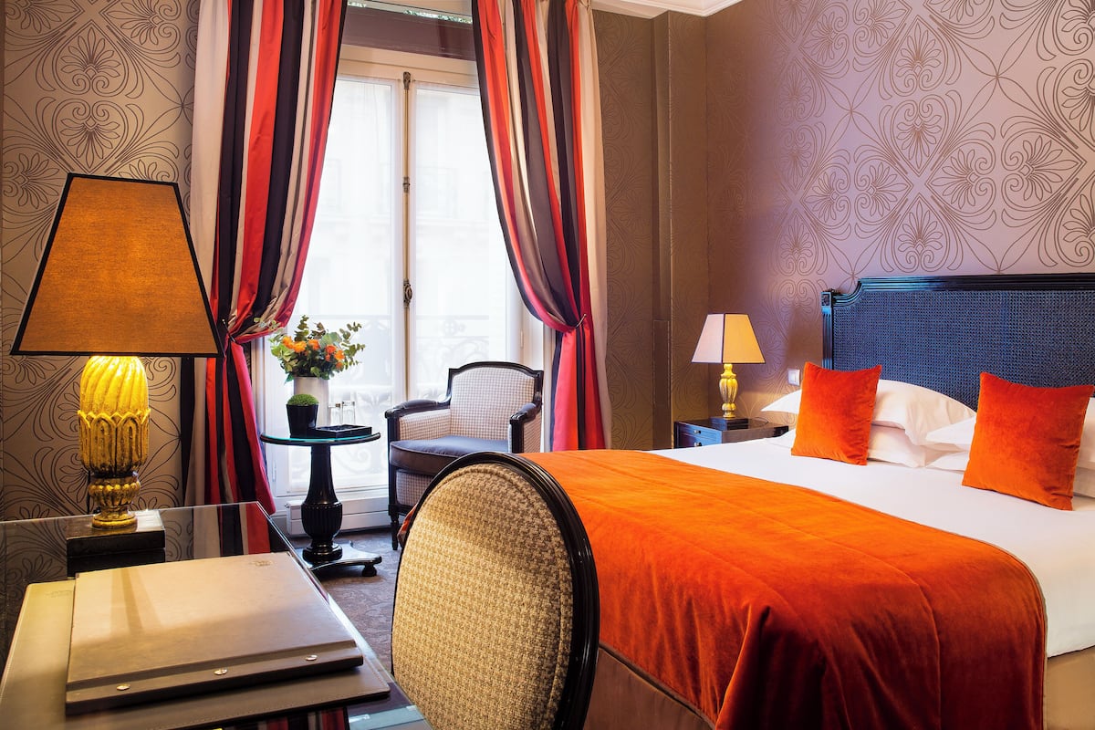 A hotel room with a large bed, two bedside tables, a chair, and a view of the outdoors through curtains.