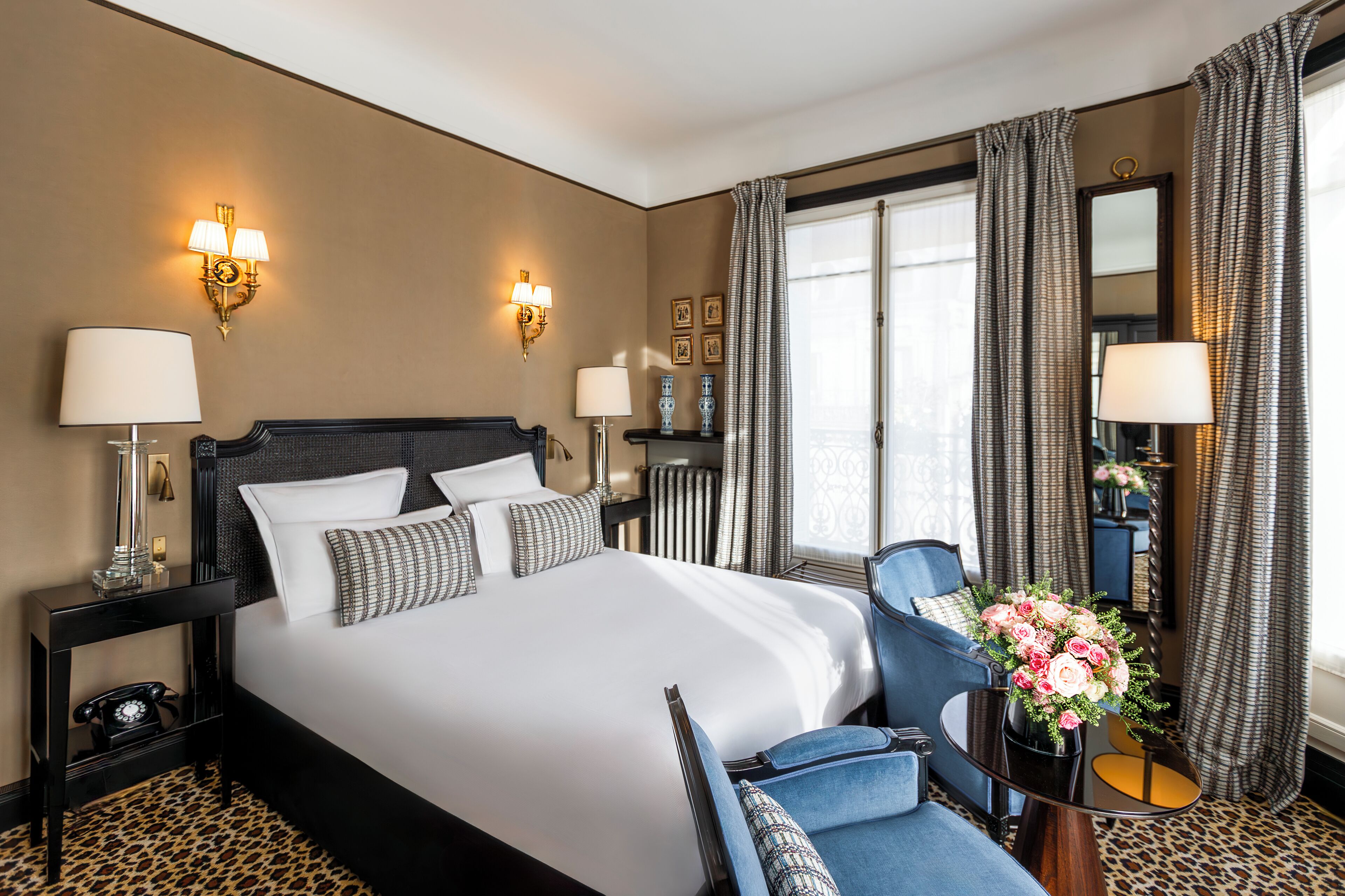 A hotel room with a large bed, a sitting area with a chair and a table, a telephone, and a vase of flowers.