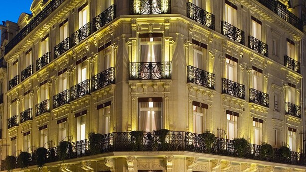 Un edificio de varios pisos con balcones ornamentales y ventanas iluminadas, presumiblemente un hotel o edificio histórico.