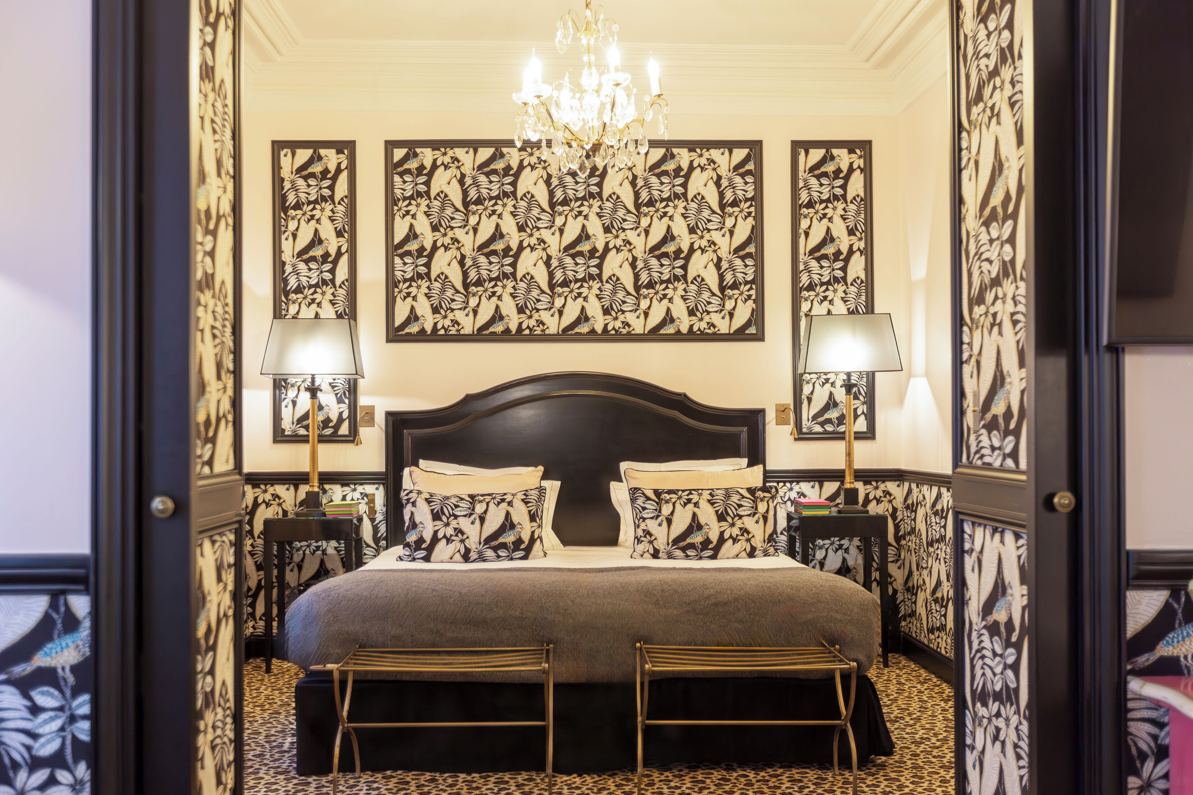 A bedroom with a large bed, two bedside tables with lamps, a chandelier, and floral wallpaper.