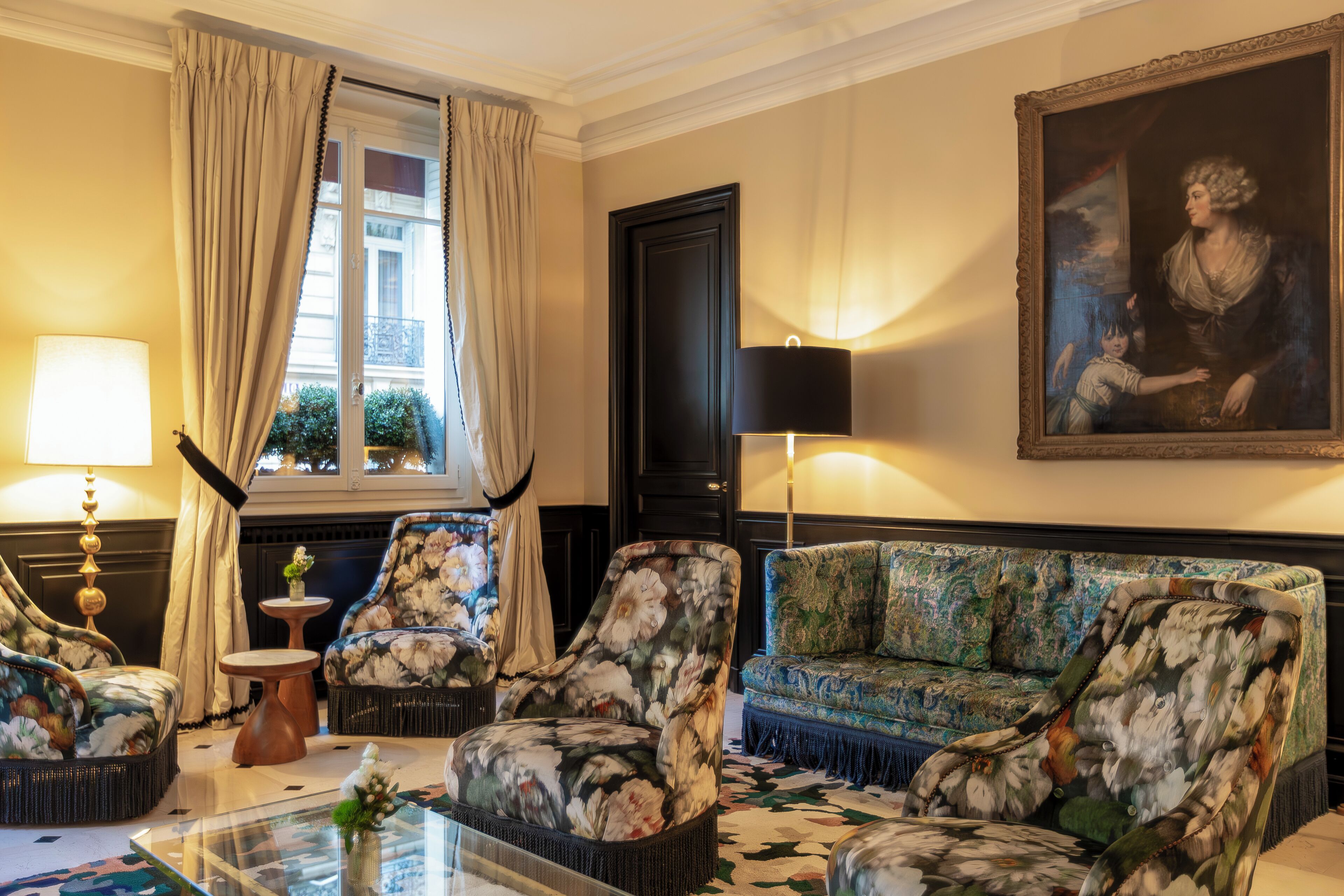 A room with a sofa, two armchairs, a glass coffee table, a lamp, and a painting on the wall.