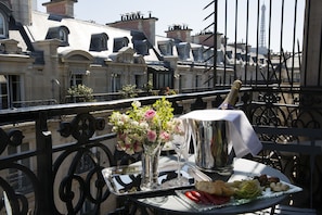 Un tavolo con una bottiglia di champagne, un vaso di fiori e un piatto di cibo su un balcone con vista su un paesaggio urbano caratterizzato da edifici storici e dalla Torre Eiffel sullo sfondo.