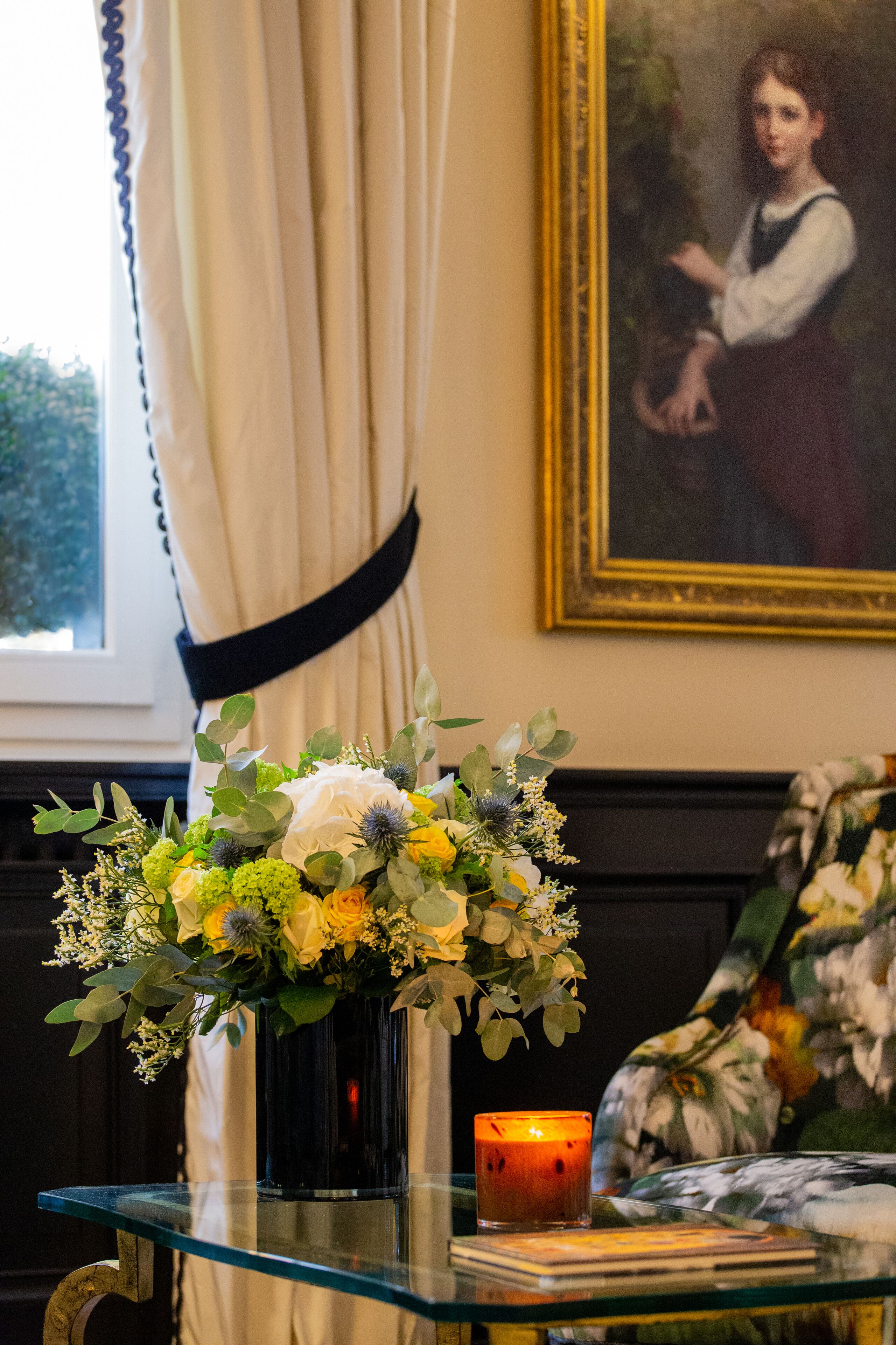 Una mesa de vidrio con un jarrón de flores, una vela y un cuadro enmarcado.