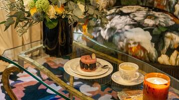 A glass table with a floral arrangement, a cake, a cup of tea, and a candle.