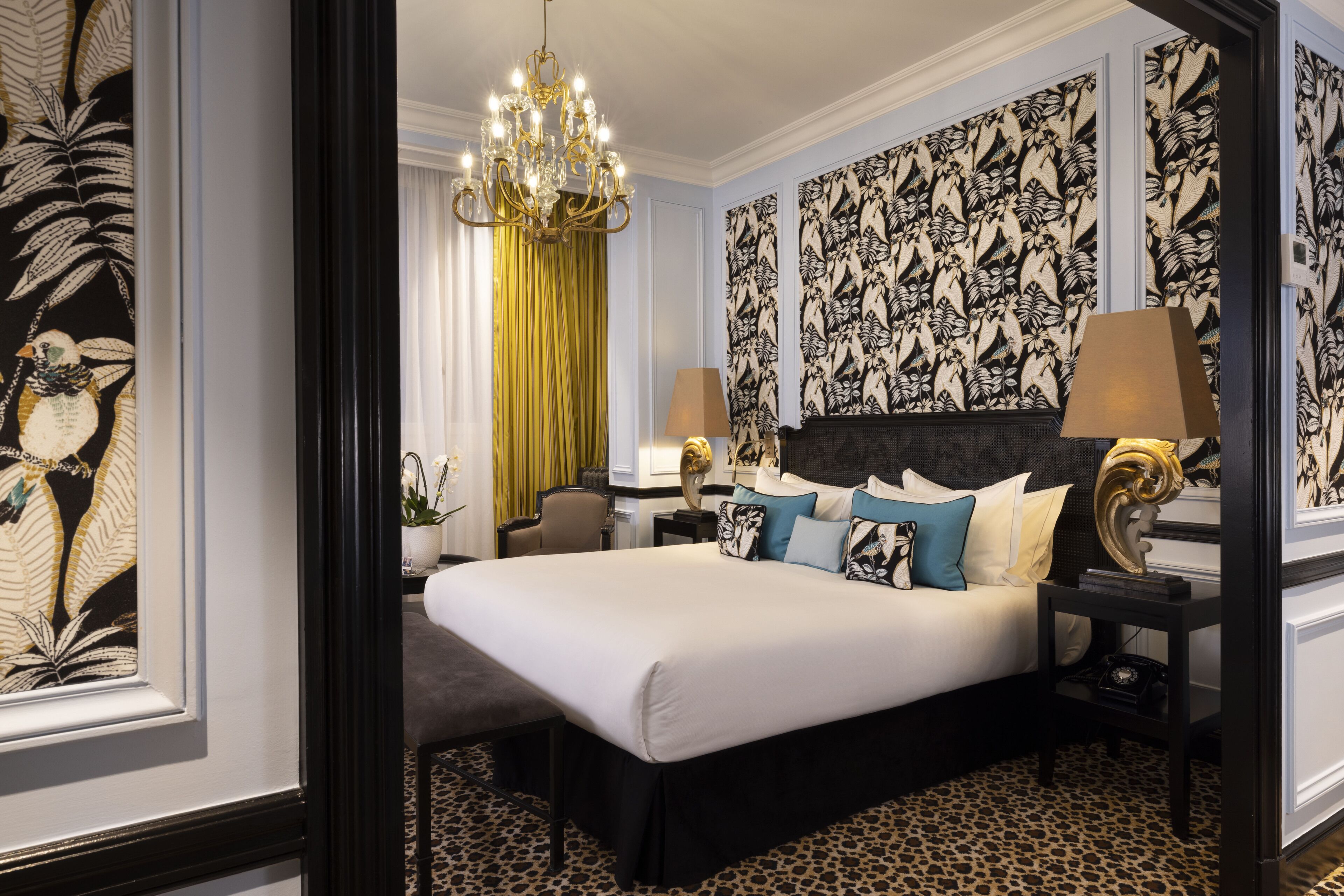 A well-appointed bedroom with a large bed, a chandelier, patterned wallpaper, and a leopard print carpet.