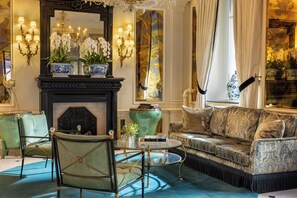 A luxurious living room with a fireplace, ornate wall sconces, and a large mirror. - West End Hotel (Paris)