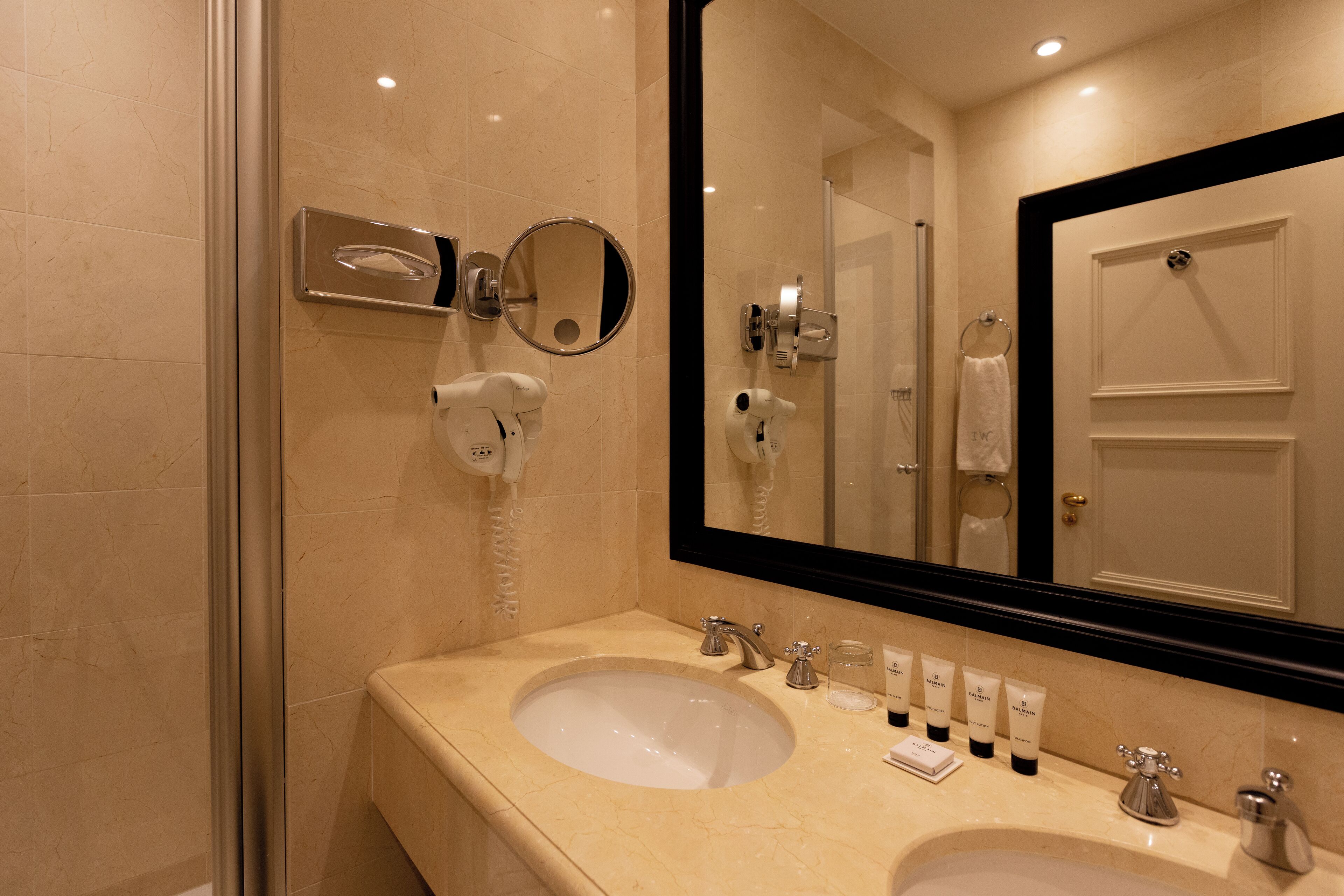 Baño de hotel con dos lavamanos, un espejo grande, un secador de pelo y un perchero para toallas.