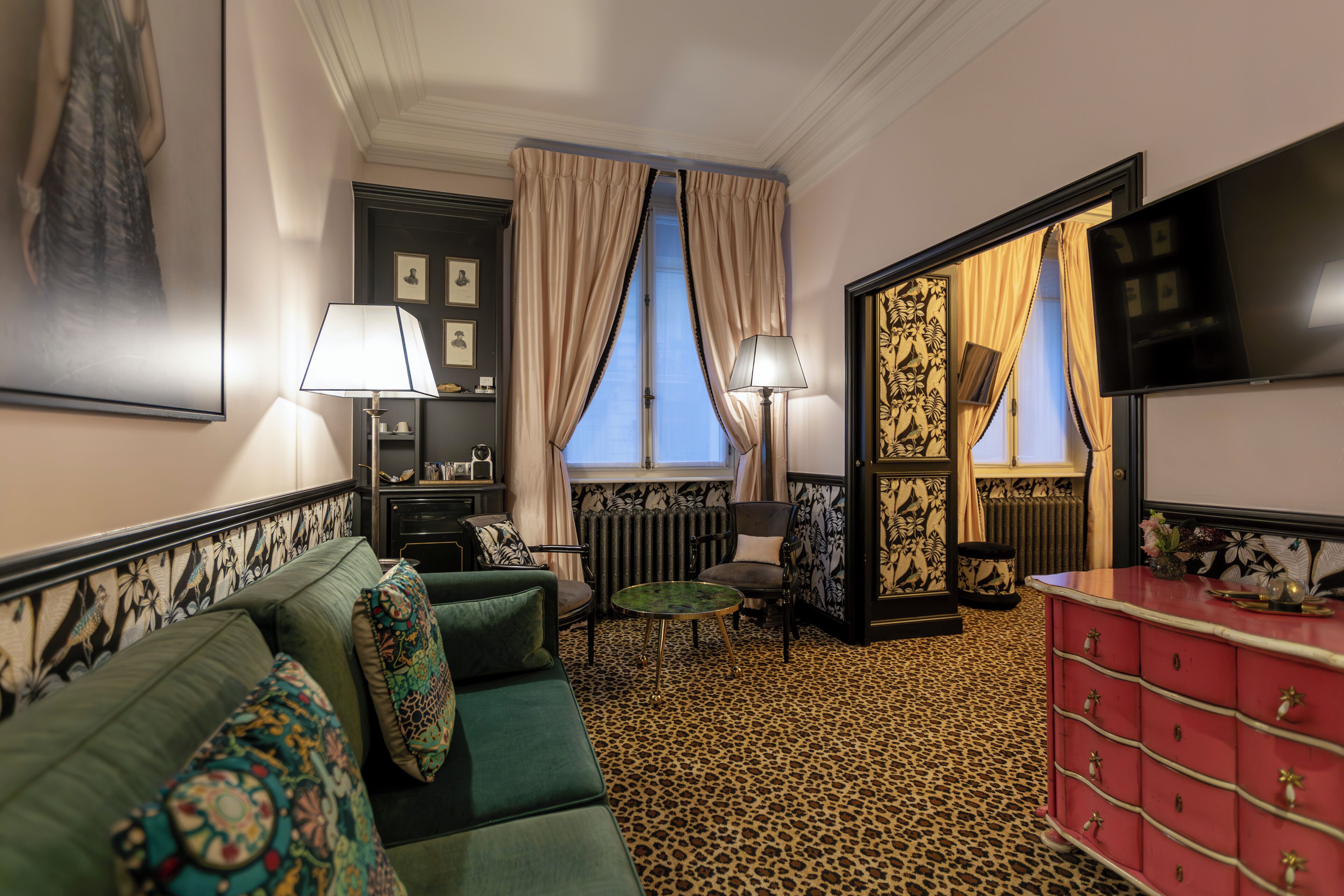 A room with a green sofa, a red dresser, a leopard print carpet, and a large window with curtains.