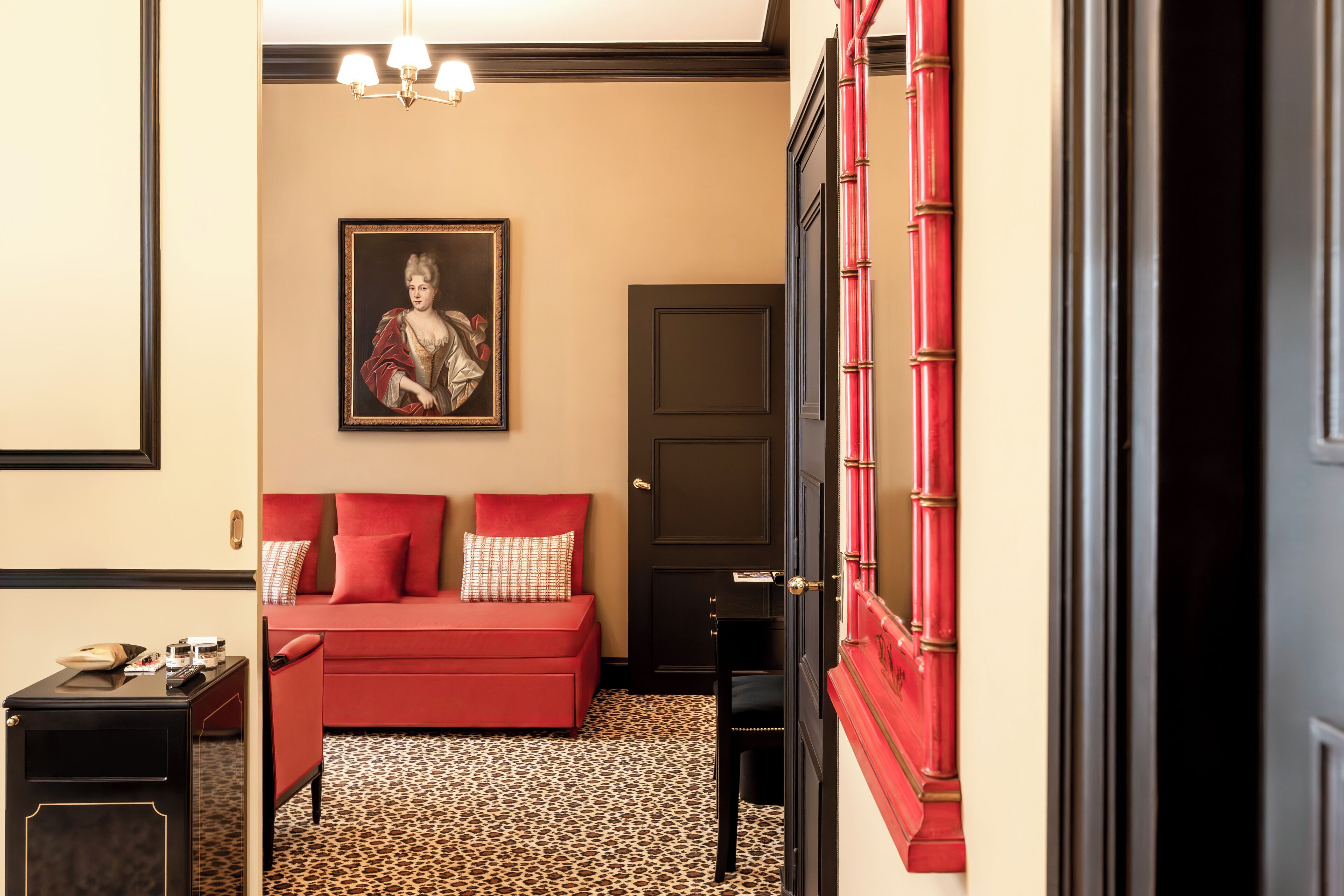 Una habitación con un sofá rojo, un retrato enmarcado en la pared, una puerta con pomos rojos y un suelo estampado.