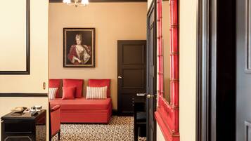 Una habitación con un sofá rojo, un retrato enmarcado en la pared, una puerta con pomos rojos y un suelo estampado.