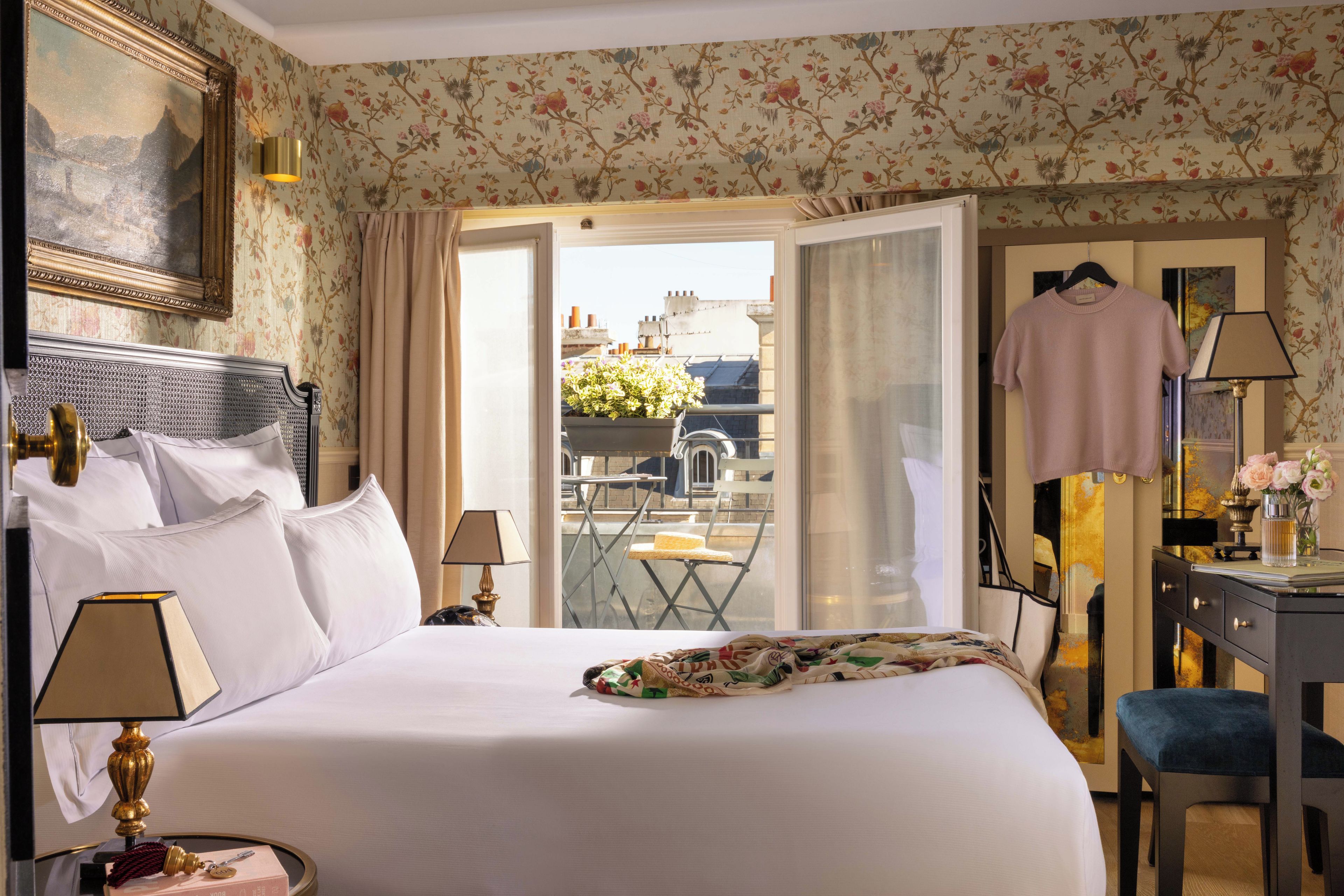 A hotel room with a bed, a desk, a chair, a hanging dress, and a view of the outside.
