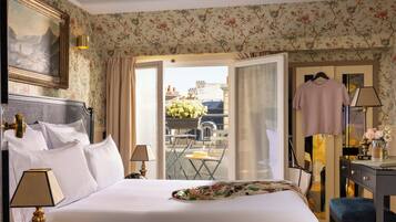 A hotel room with a bed, a desk, a chair, a hanging dress, and a view of the outside.