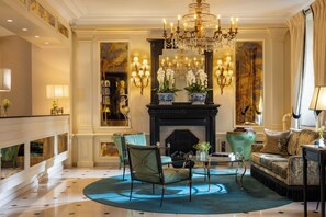 A luxurious living room with a grand chandelier, ornate wall sconces, a fireplace, and classic furniture. - West End Hotel (Paris)