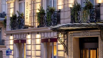 Fachada de hotel con un letrero que dice "West-End Hotel", balcones con plantas y un toldo de hierro forjado.
