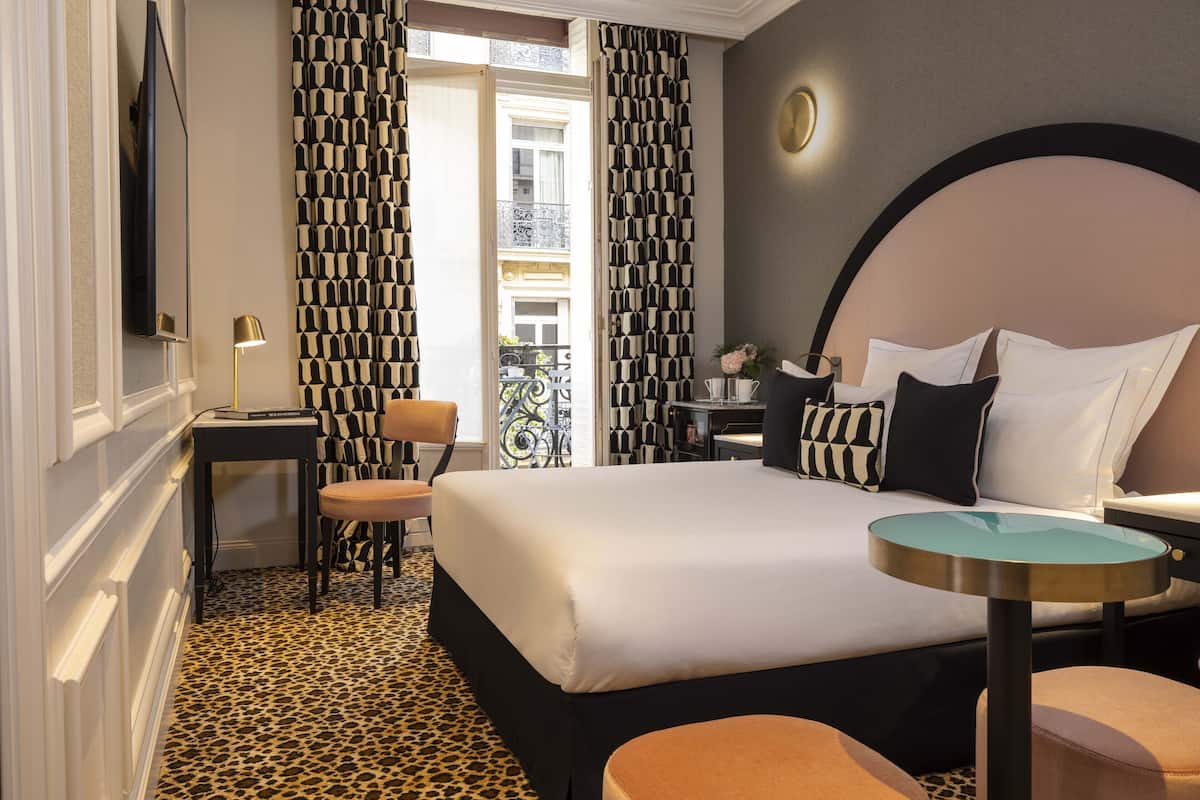 A hotel room with a large bed, a round table, a chair, and a balcony view.