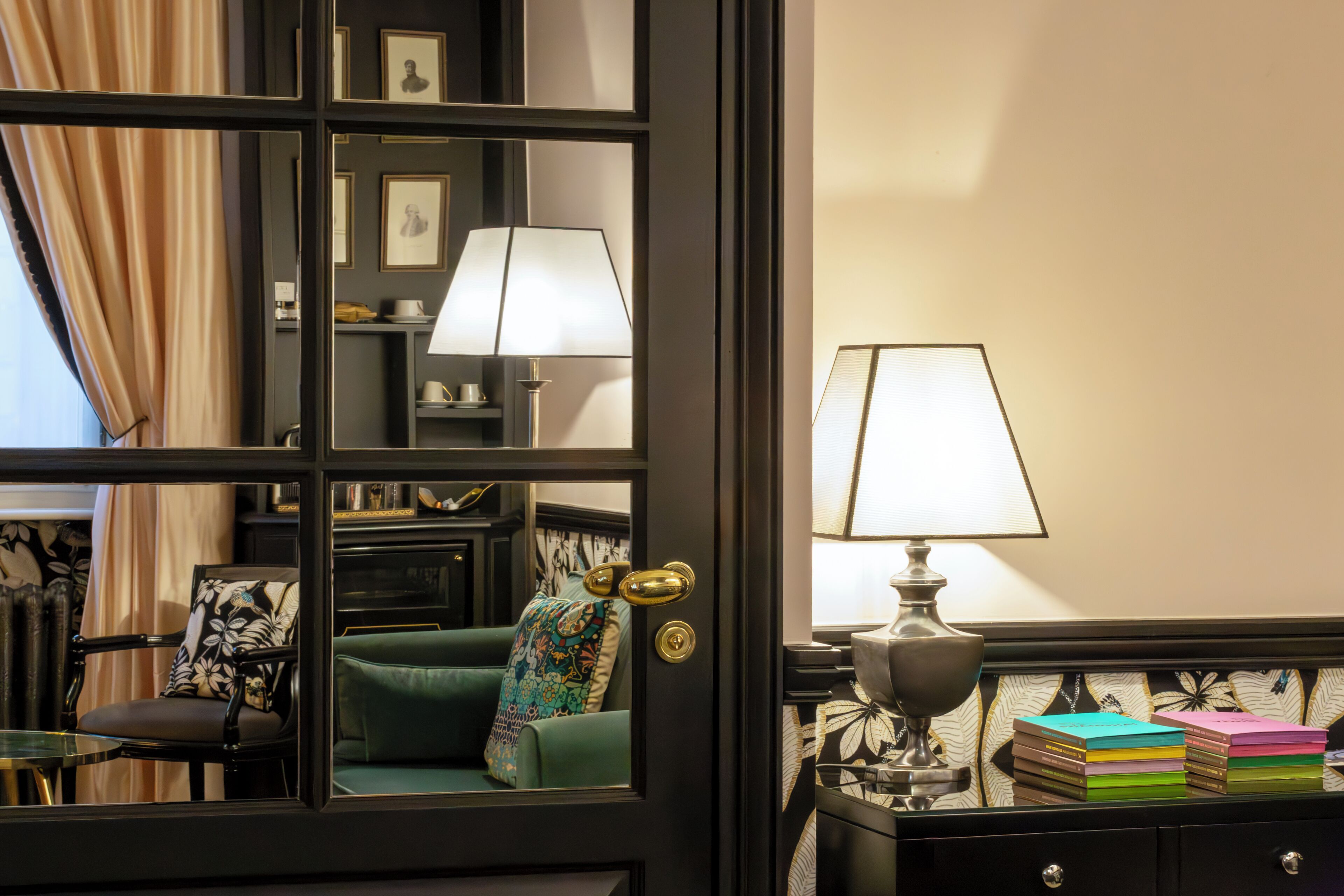 Una habitación con un sofá verde, un sillón con cojín estampado, un escritorio con lámpara y cuadros en la pared.