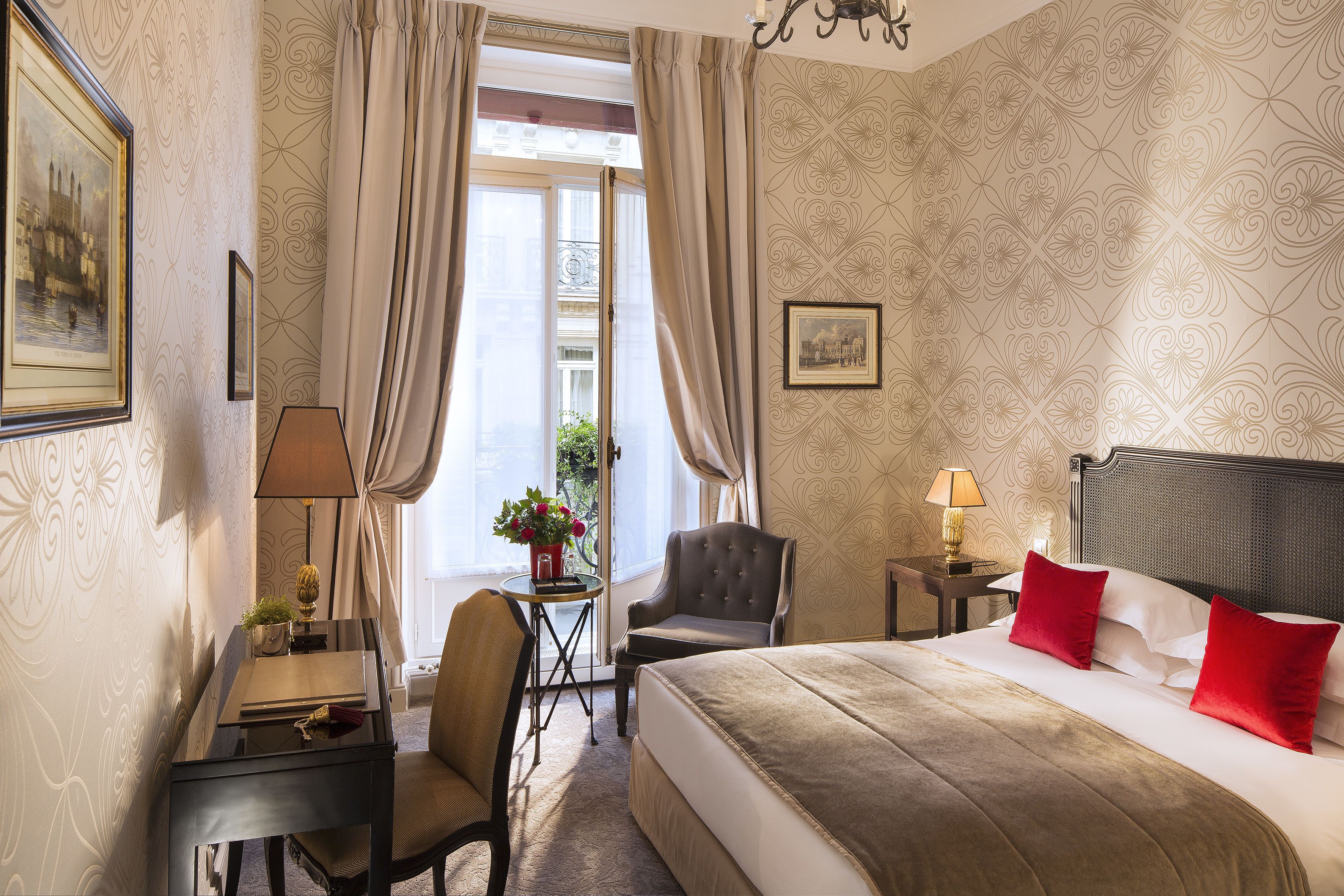 A hotel room with a bed, a desk, a chair, a small table with a lamp, and a window with curtains.