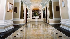 A spacious hallway with a polished marble floor, white walls, and a decorative ceiling with lights.