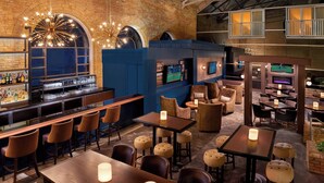 A bar area with stools, tables, and a television screen.