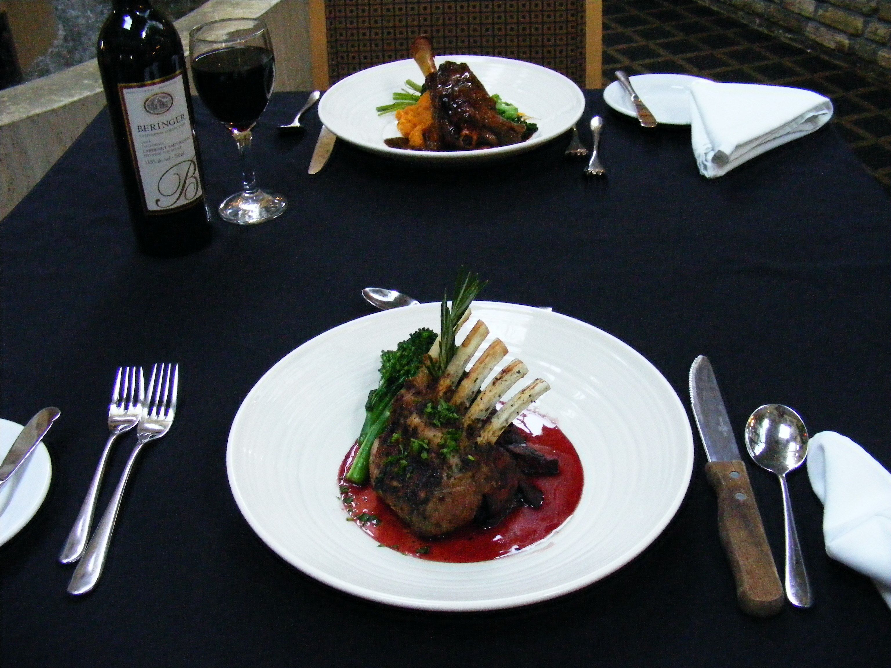 A table set with a bottle of wine, two plates of food, cutlery, and a folded napkin.