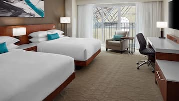 A hotel room with two beds, a desk, a chair, and a large window with a view of a building.