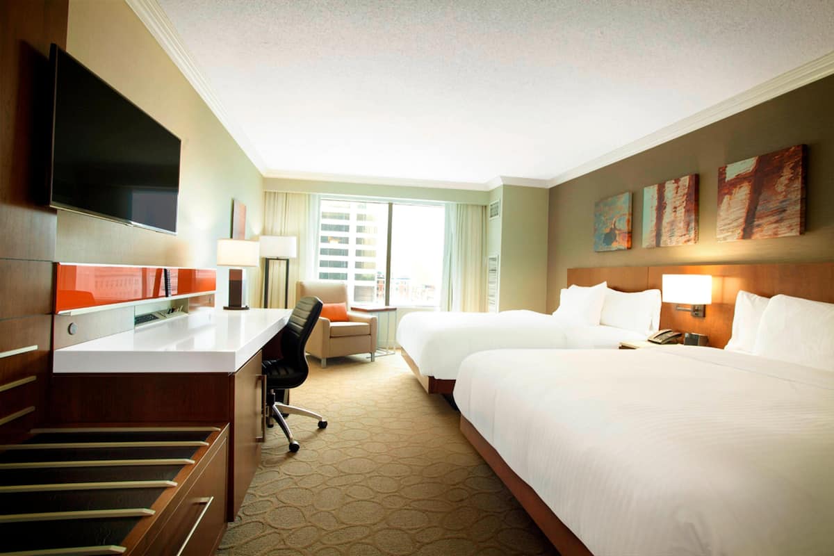 A hotel room with a bed, desk, chair, TV, and artwork on the walls.