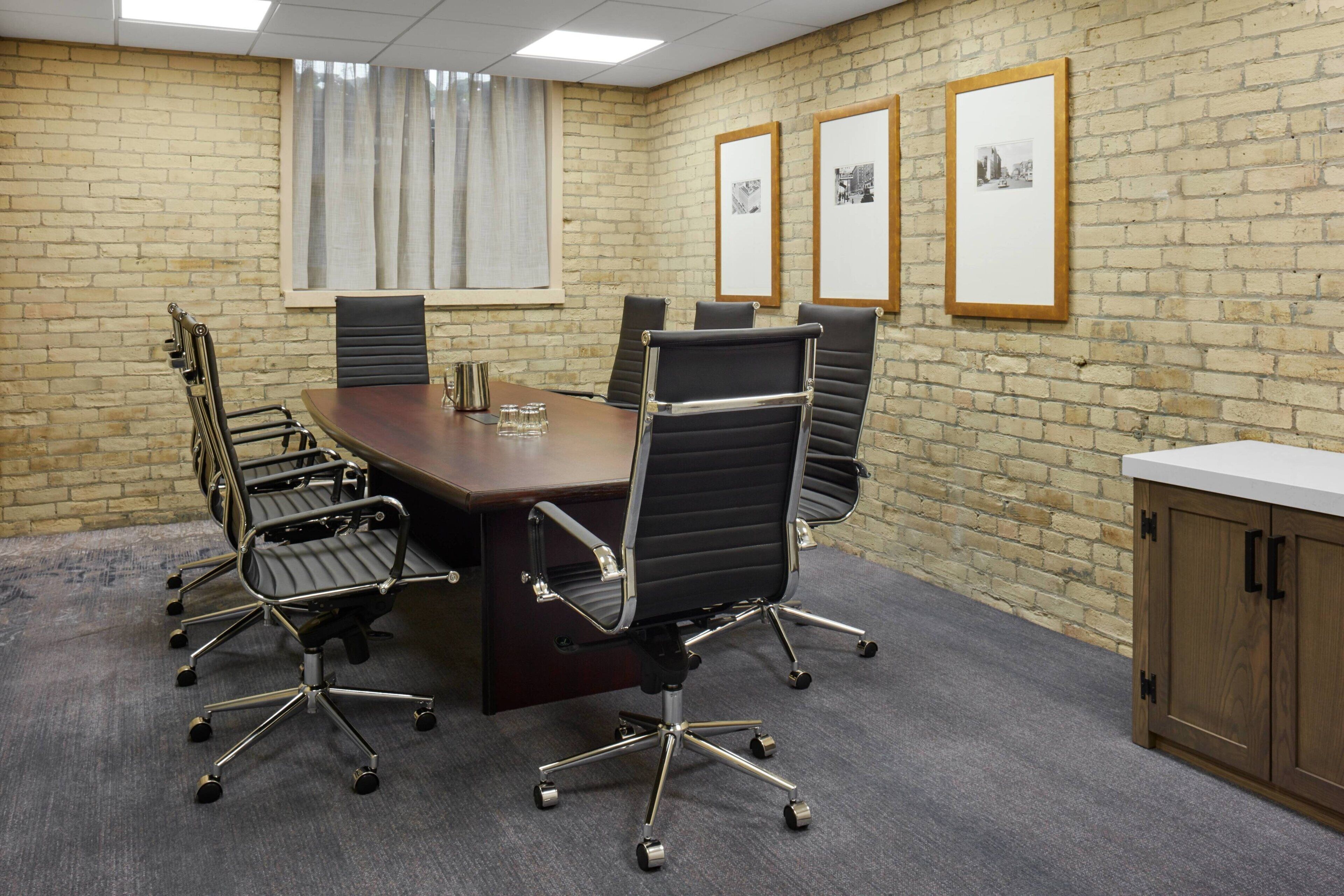 A conference room with a brick wall, a large table, and six office chairs.