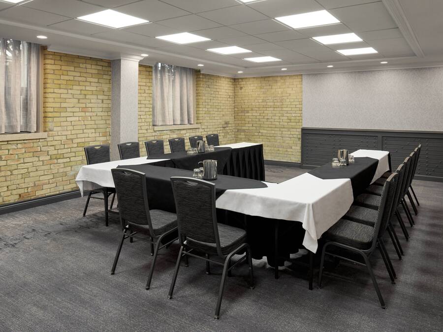 Uma sala de conferência com parede de tijolos, uma mesa grande com cadeiras e piso coberto por carpete cinza.