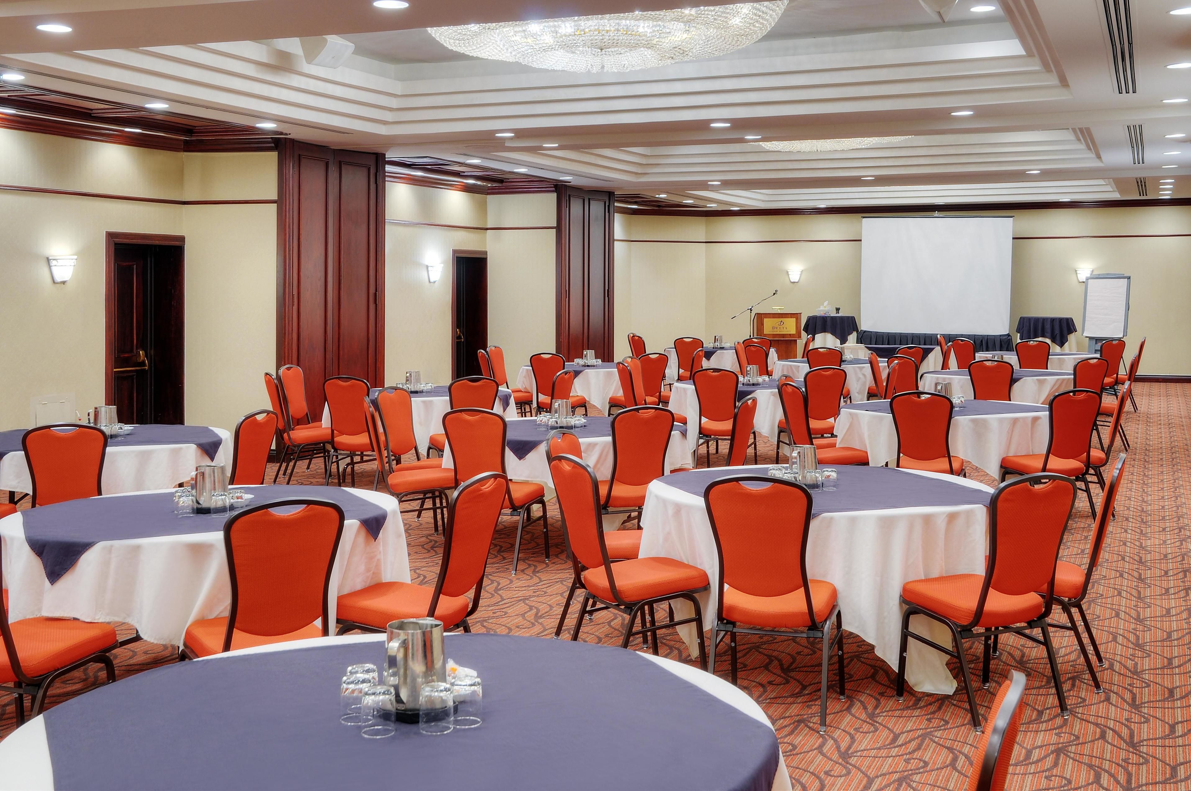 A conference room with multiple tables and orange chairs, equipped with nameplates and water glasses.