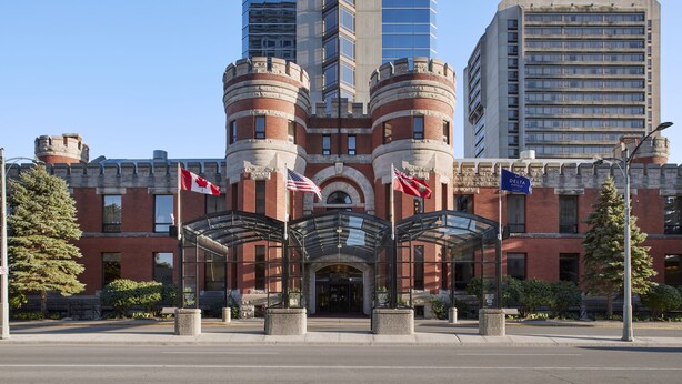 A hotel with a central entrance, two flagpoles with flags, and a glass canopy over the entrance.