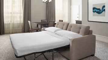 Una habitación de hotel con cama, una mesa de comedor, sillas, una araña y una obra de arte enmarcada en la pared.