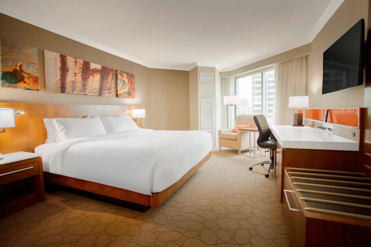 A hotel room with a large bed, a desk, a chair, a TV, and artwork on the walls.