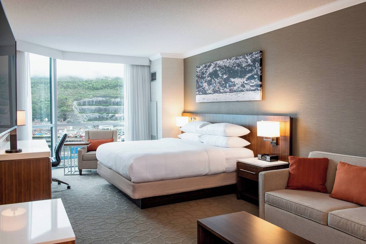 Una habitación de hotel con una cama grande, un escritorio, una silla, un sofá y vistas a la ciudad.