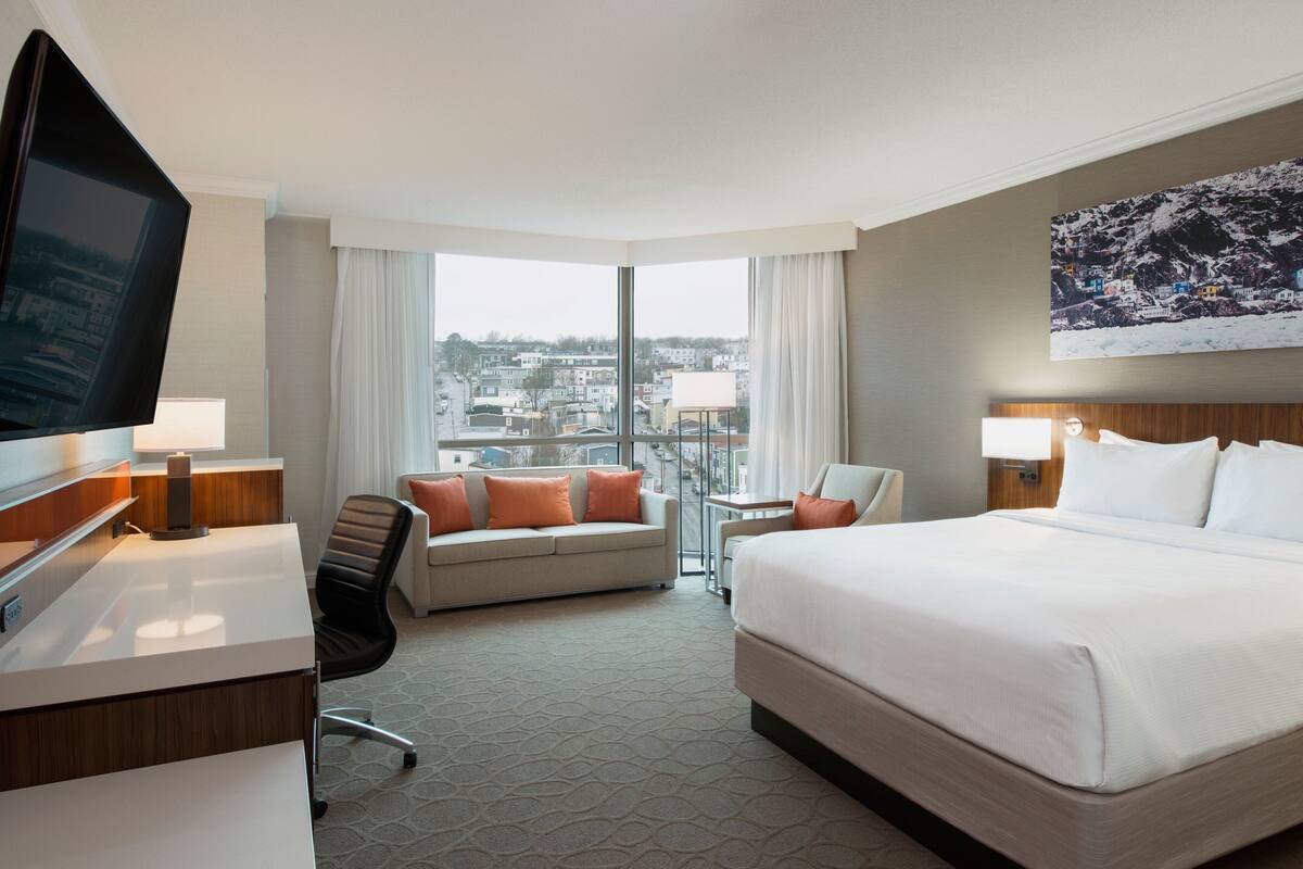 Habitación de hotel con una cama grande, un escritorio, un sofá, un televisor y vistas a la ciudad a través de la ventana.