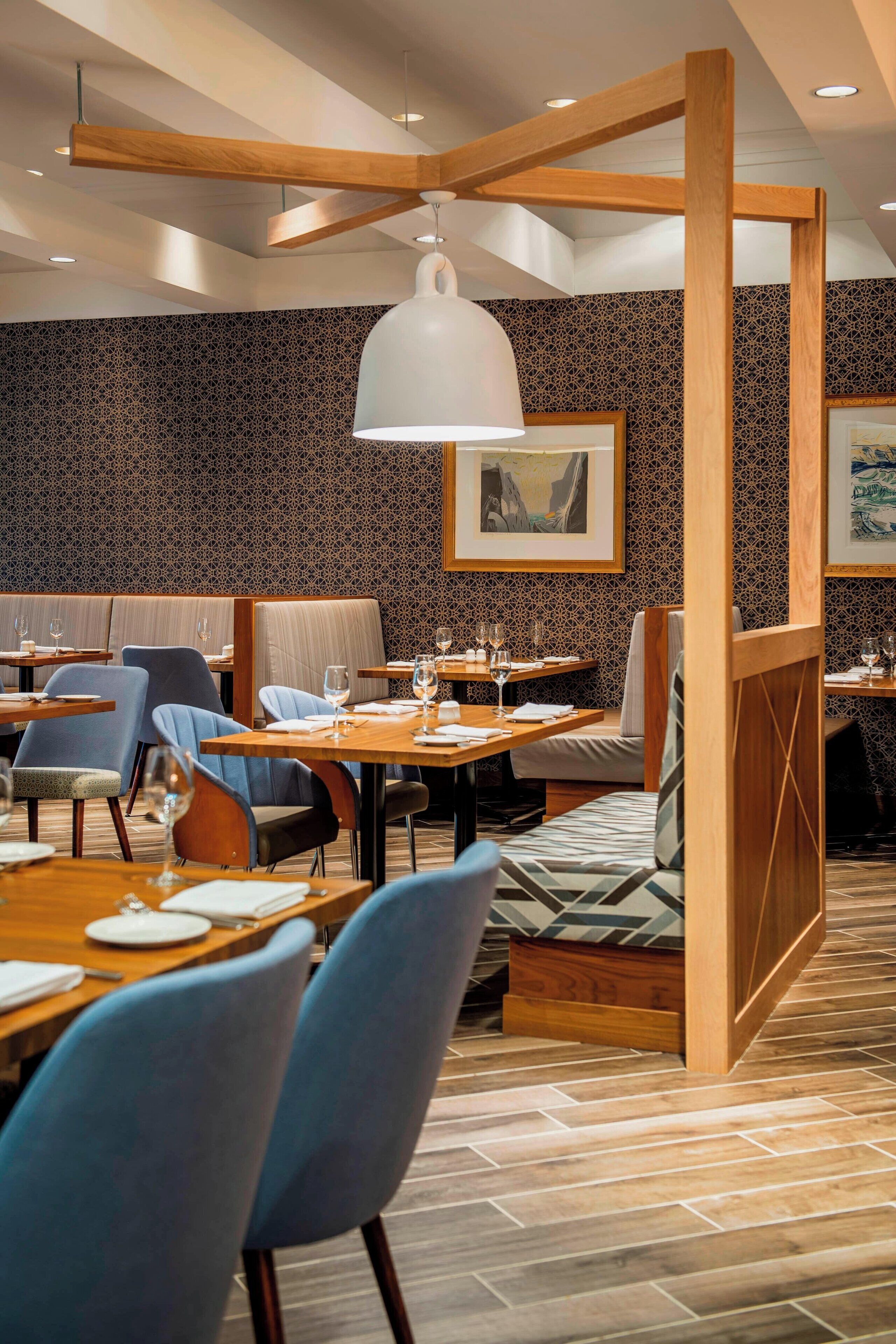 A restaurant with wooden tables, blue chairs, and patterned walls.