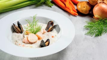 A bowl of seafood soup garnished with herbs, surrounded by vegetables like carrots and potatoes.