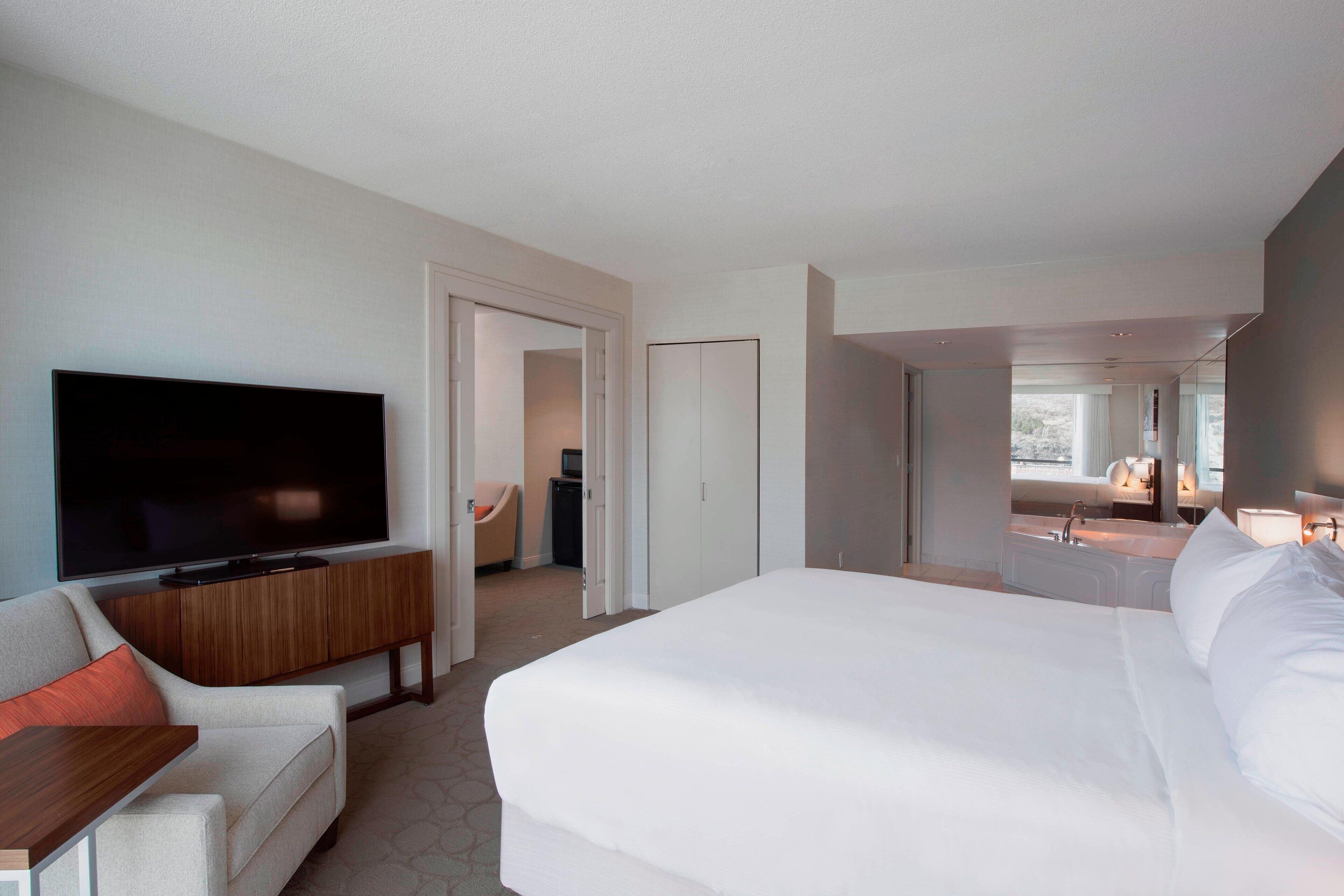 Quarto de hotel com uma cama grande, televisão, sofá e banheiro visível por uma porta aberta.