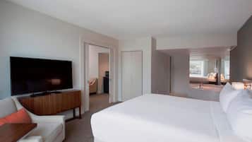 Quarto de hotel com uma cama grande, televisão, sofá e banheiro visível por uma porta aberta.