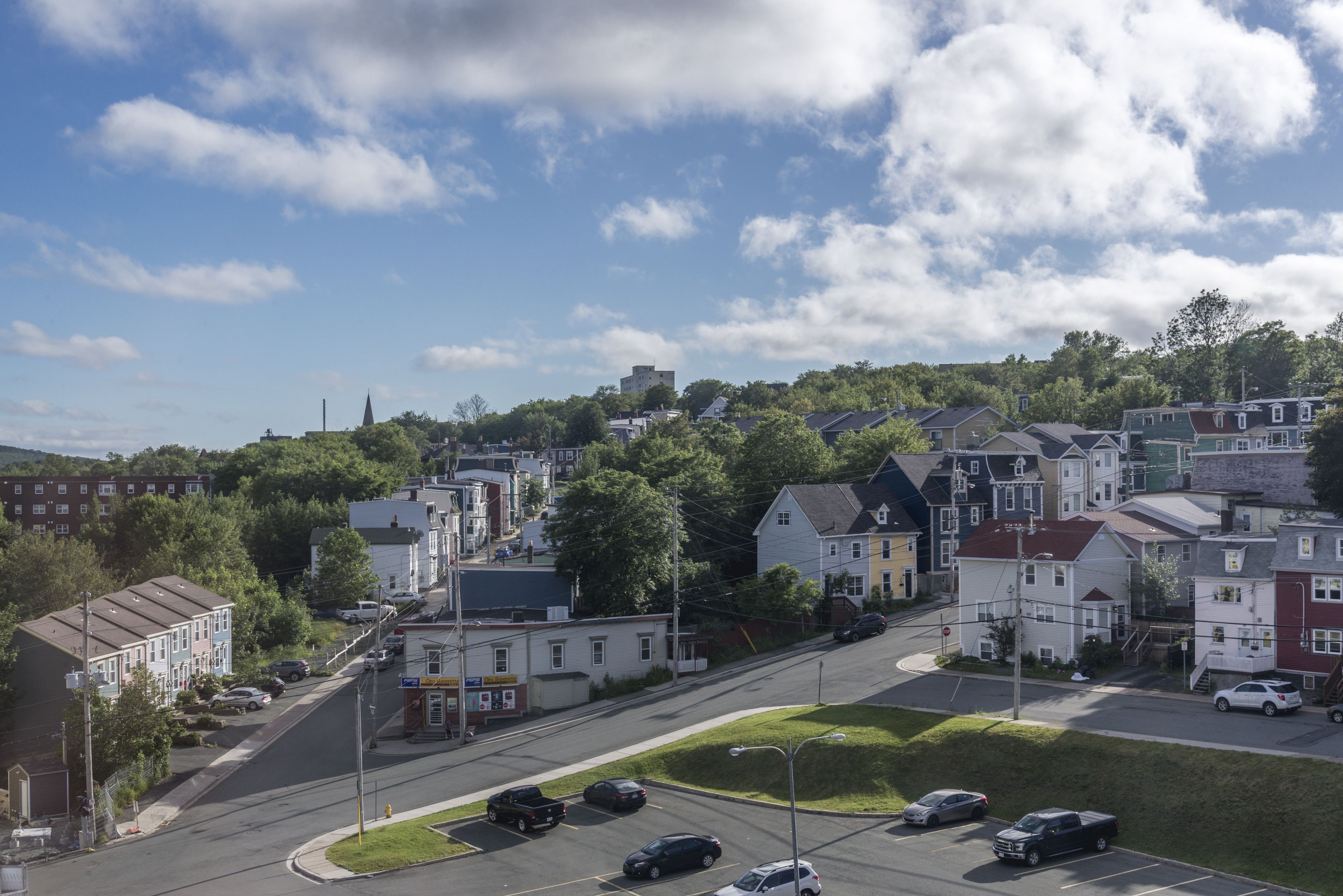 A residential street with houses, parked cars, and a clear sky.