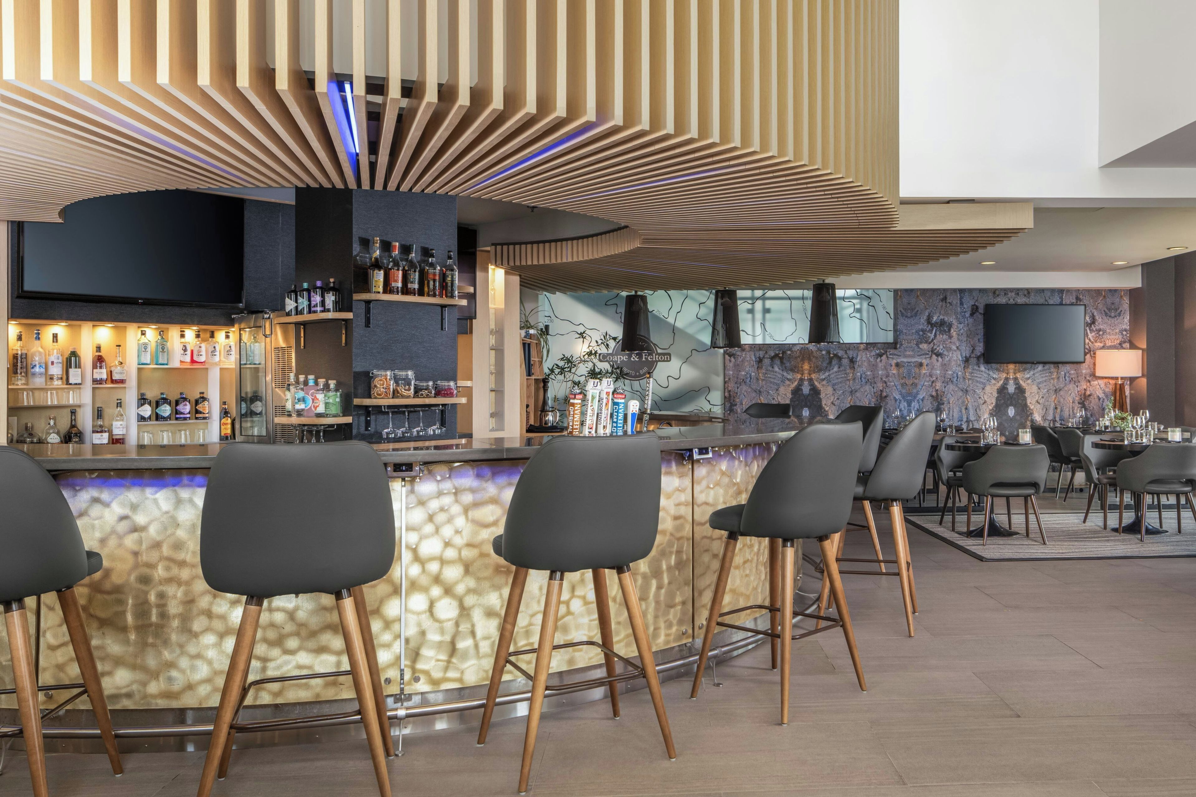 Un área de bar moderna con una barra curva, taburetes y una variedad de botellas de licor.