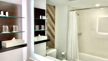Un baño moderno con cabina de ducha de vidrio, un inodoro con dispensador de toallas de papel y estantes con artículos de tocador.