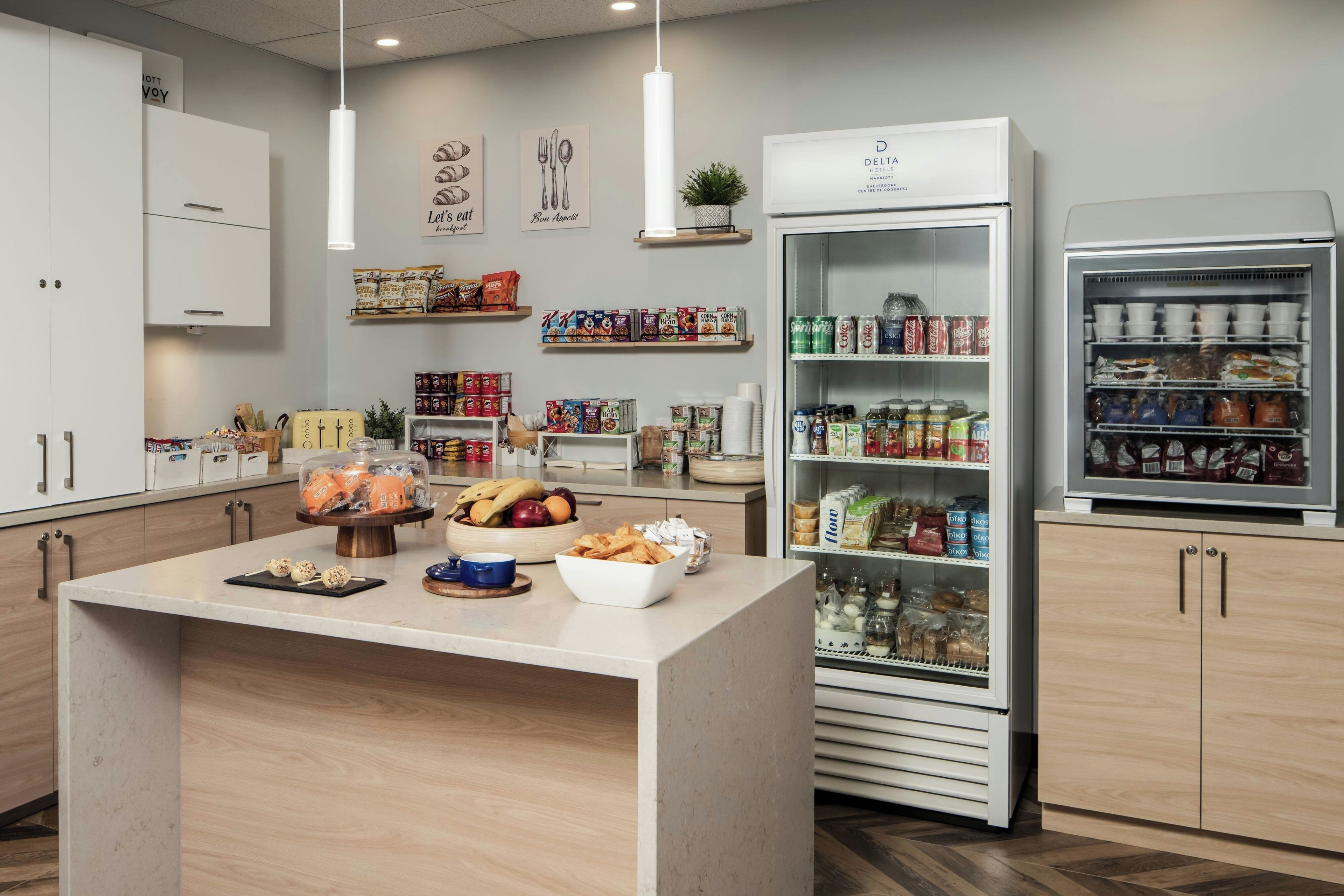 Une cuisine d’hôtel dotée d’un îlot central, de divers produits alimentaires et d’un réfrigérateur rempli de boissons.