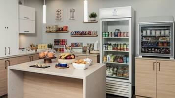 Une cuisine d’hôtel dotée d’un îlot central, de divers produits alimentaires et d’un réfrigérateur rempli de boissons.