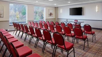 A conference room with rows of red chairs, a large table, and a flat-screen TV on the wall.